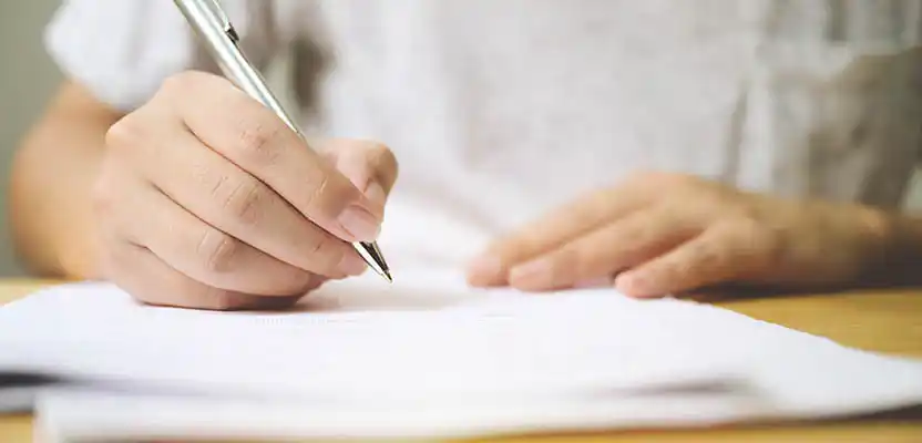 A hand holding a pen shows someone filling out the TA6 Property Information form.